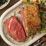 Horseradish-crusted prime rib, sliced on a white platter and served with roasted garlicky cauliflower and sauteed spinach.