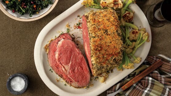 Horseradish-crusted prime rib, sliced on a white platter and served with roasted garlicky cauliflower and sauteed spinach.