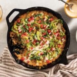 Ground Beef Cheesy Dip in cast iron pan on table next to bowl of tortilla chips and queso.