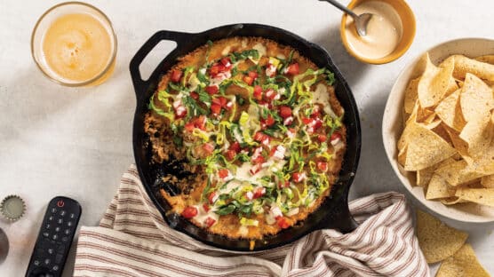 Ground Beef Cheesy Dip in cast iron pan on table next to bowl of tortilla chips and queso.