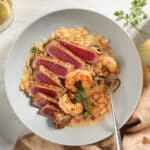 Elegant place setting with white bowl featuring pan-seared tuna with coconut shrimp and brown rice served with a glass of white wine.