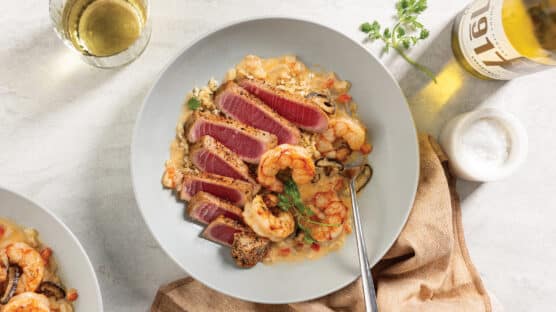 Elegant place setting with white bowl featuring pan-seared tuna with coconut shrimp and brown rice served with a glass of white wine.