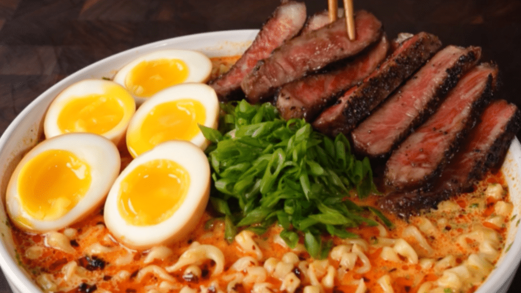 Bowl with ramen noodles in a creamy sauce and topped with marinated egg halves, diced green onions and sliced Wagyu steak.