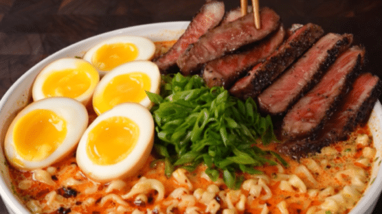 Bowl with ramen noodles in a creamy sauce and topped with marinated egg halves, diced green onions and sliced Wagyu steak.