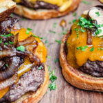 Two butter burgers topped with American cheese, caramelized onions, and garlic aioli on a rustic wood counter.