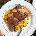 person holding white plate with sliced Pan-Seared Ribeye Crown Steak with Tomato Basil Fondue and Saffron Risotto