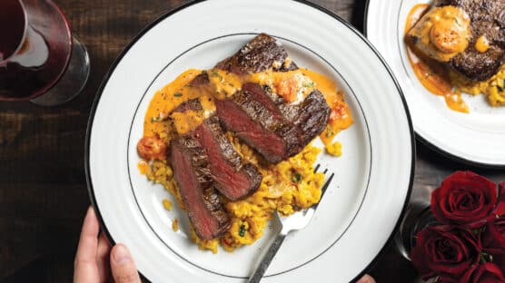 person holding white plate with sliced Pan-Seared Ribeye Crown Steak with Tomato Basil Fondue and Saffron Risotto