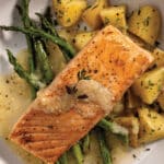 Broiled Salmon With Asparagus, Buttered Potatoes, and White Wine & Lemon Butter Finishing Sauce on a white plate