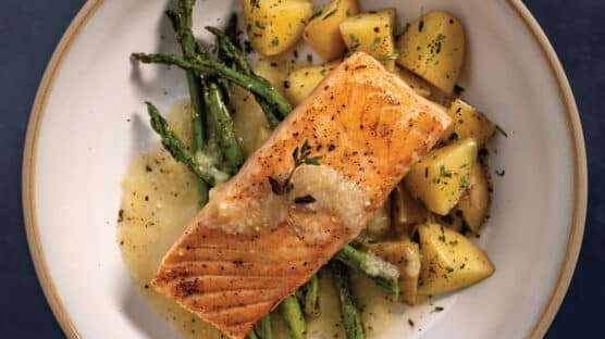 Broiled Salmon With Asparagus, Buttered Potatoes, and White Wine & Lemon Butter Finishing Sauce on a white plate