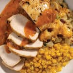 Pan-Seared Chicken With Cheesy Potatoes, Creamed Corn, and Creamy Tomato & White Wine Finishing Sauce on a white plate