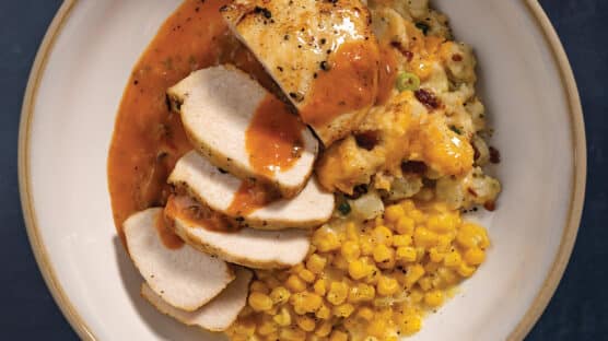 Pan-Seared Chicken With Cheesy Potatoes, Creamed Corn, and Creamy Tomato & White Wine Finishing Sauce on a white plate