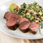 White plate with slices of bistro steak cooked medium-rare served with a southwest salad.