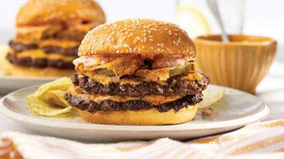 White plate with burger with 2 smash burger patties, 2 slices cheese, fried green tomatoes and melty pimento cheese.