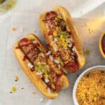 Two bacon-wrapped franks loaded with toppings and a crispy tortilla chip crumble.