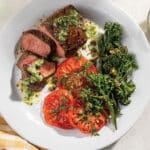 Grilled Top Sirloin With Chimichurri Butter and Grilled Broccolini With Caper Vinaigrette and Heirloom Tomatoes on a white plate