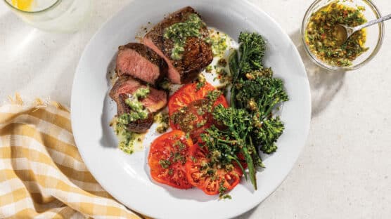 Grilled Top Sirloin With Chimichurri Butter and Grilled Broccolini With Caper Vinaigrette and Heirloom Tomatoes on a white plate