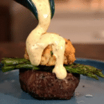 Pouring Bearnaise sauce over filet mignon topped with asparagus and crab cake
