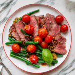 White plate with green beans, blistered tomatoes and sliced filet mignon cooked medium-rare.