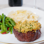 White plate with parmesan-herb crusted filet mignon, green beans, and mashed potatoes.