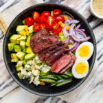 Black bowl with salad topped with sliced filet mignon