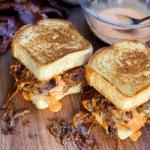2 thick patty melts on a cutting board with dressing in a bowl in the background