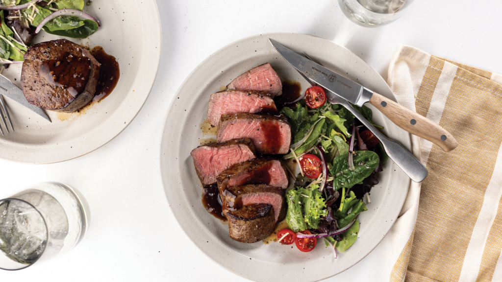 Spooning a balsamic pan sauce over a cooked Omaha Steaks USDA Certified Very Tender filet mignon steak.