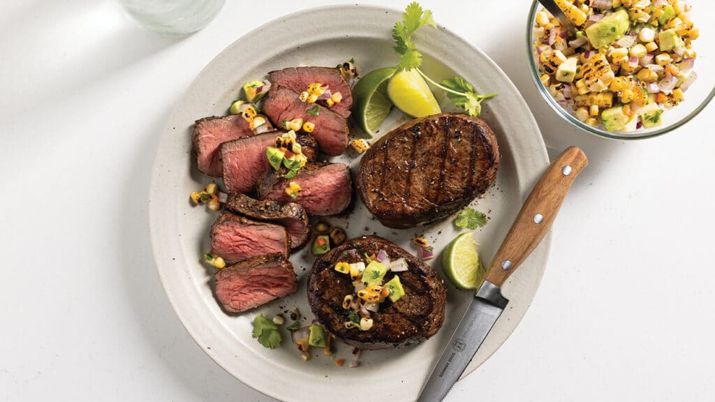 White plate with 3 grilled top sirloin filet steaks with corn and avocado salsa