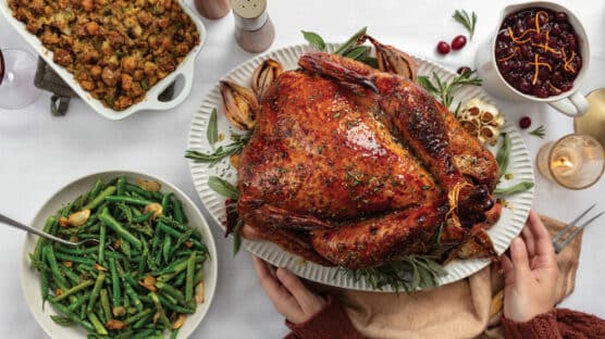 Thanksgiving table with cooked whole turkey, bowl of green bowls, sausage and cranberry dressing, and bowl of cranberry sauce
