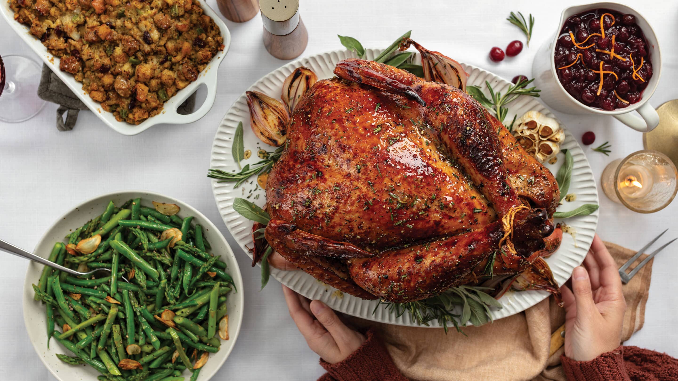 Thanksgiving table with cooked whole turkey, bowl of green bowls, sausage and cranberry dressing, and bowl of cranberry sauce