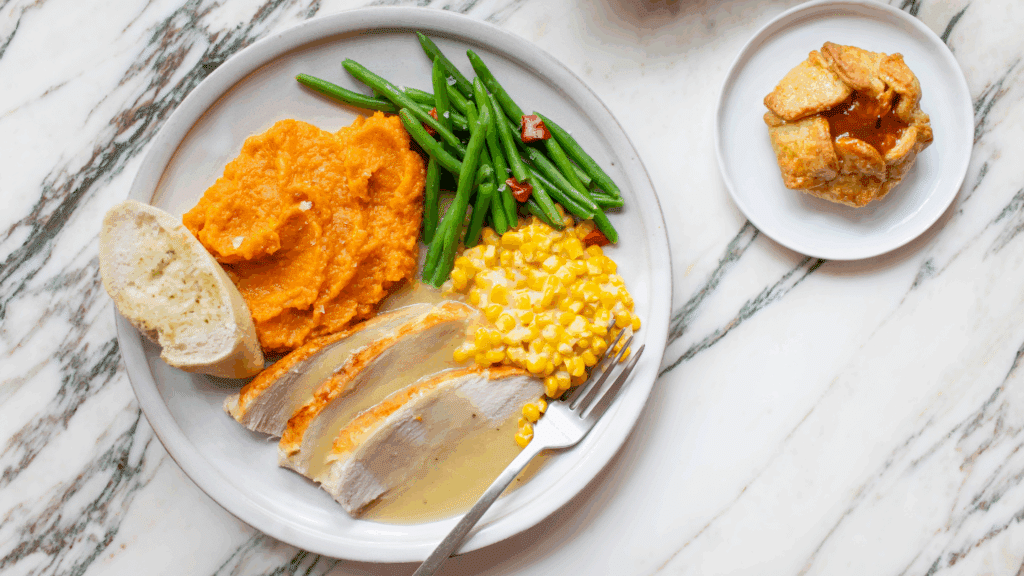 Thanksgiving plate with sliced turkey with gravy, corn, whipped sweet potatoes, green beans, and caramel apple tartlet.