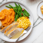 Thanksgiving plate with sliced turkey with gravy, corn, whipped sweet potatoes, green beans, and caramel apple tartlet.