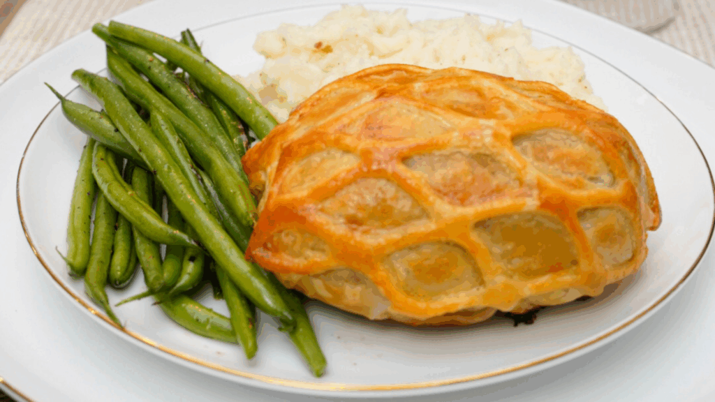 White plate with individual beef wellington, green beans and mashed potatoes.