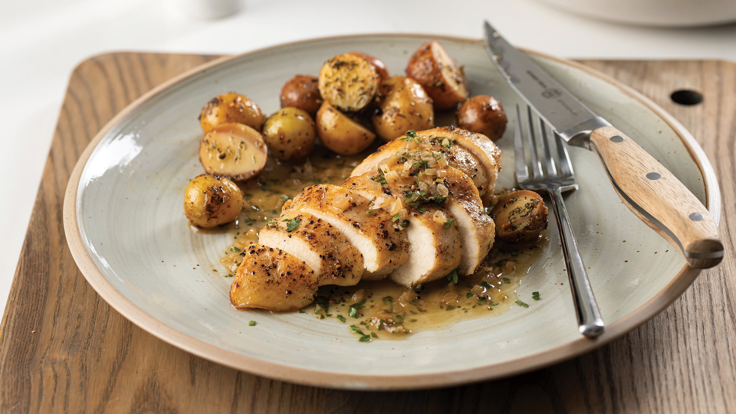 Grey plate with pan-seared chicken and roasted potatoes with pan sauce