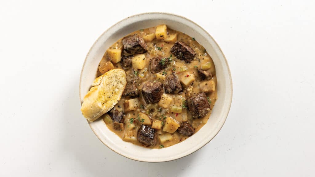steak and potato soup in a white bowl with a piece of garlic bread