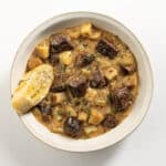 steak and potato soup in a white bowl with a piece of garlic bread